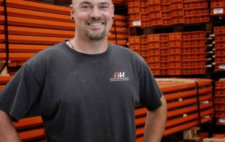 AK Employee James Jungbauer stands in front of piles of pallet rack beams stacked on top of eachother