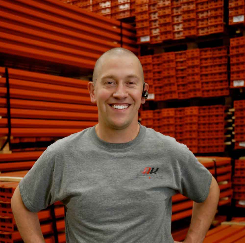 AK Employee Eric Dutcher stands in front of piles of pallet rack beams stacked on top of eachother