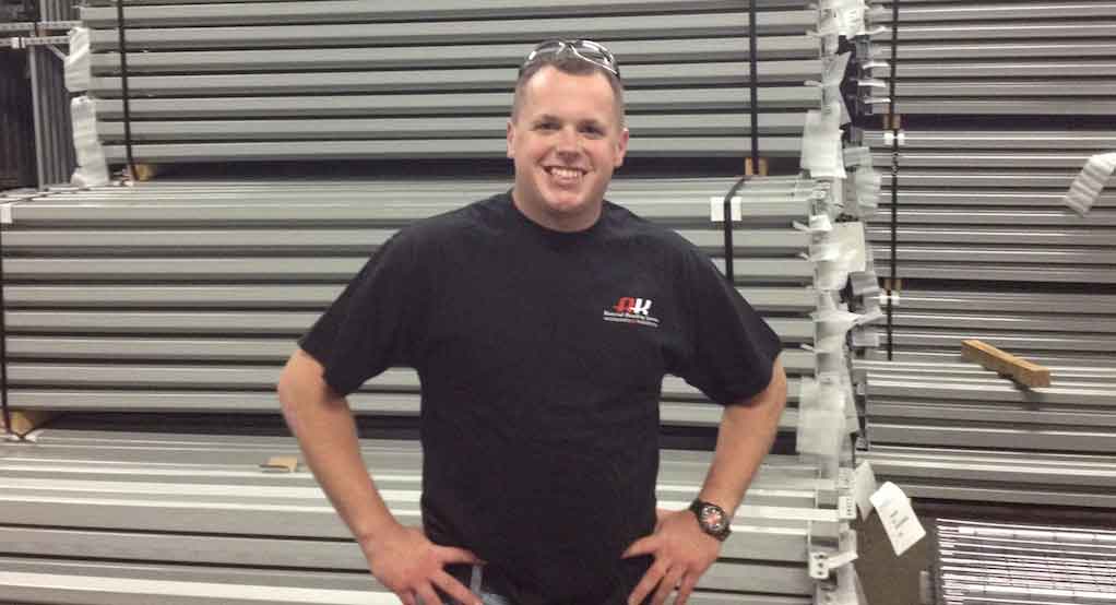 AK Employee Matt Johnson smiles with his hands on his hips standing in front of pallet rack frames