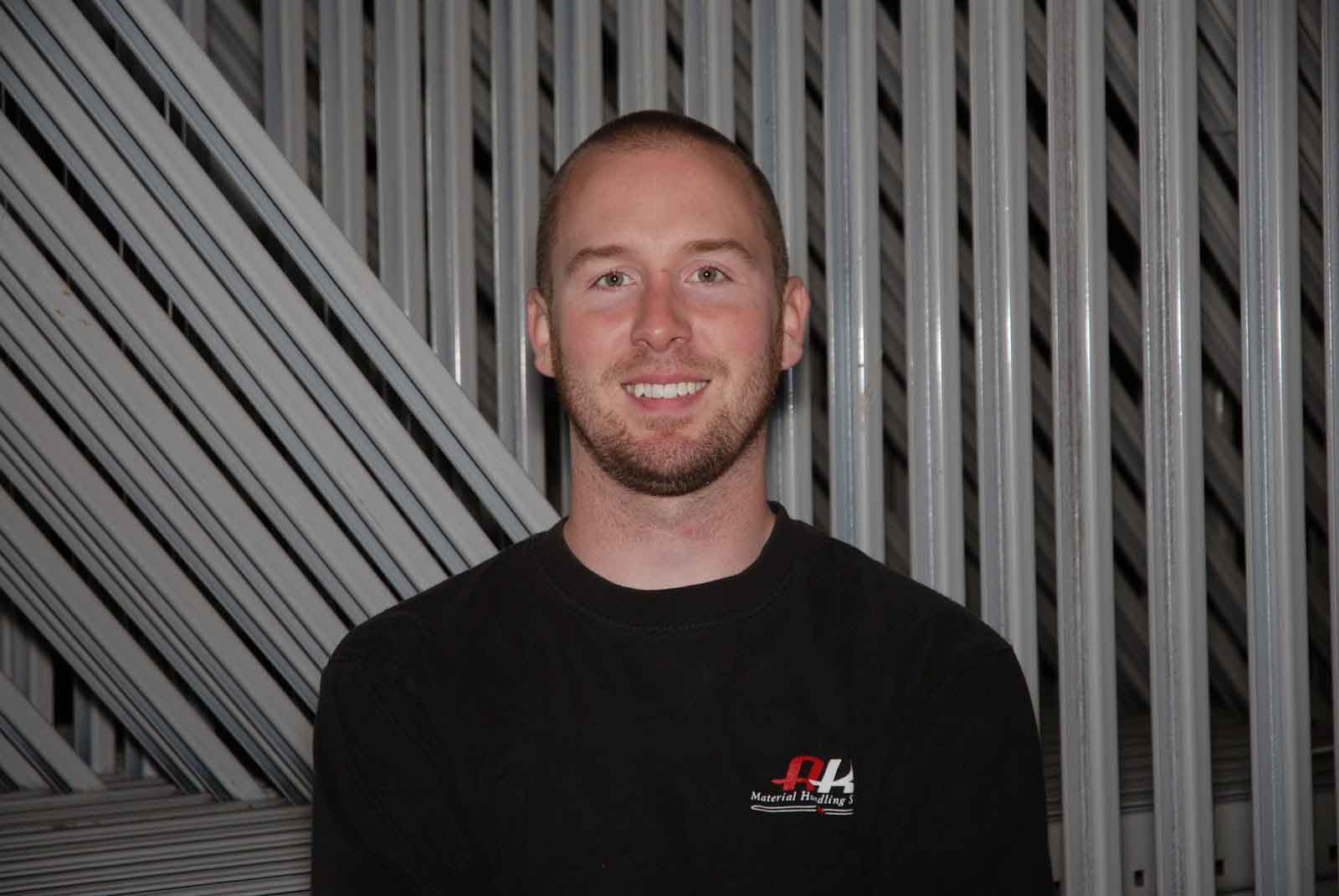 AK Employee Shawn Jones stands and smiles in front of pallet rack beams