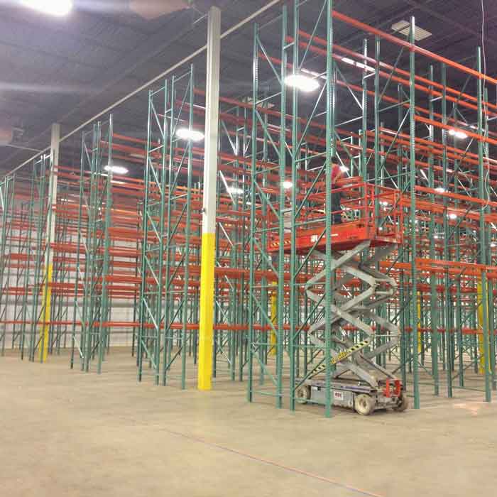 a person stands on a mobile work patfomr in a warehouse filled with pallet rack bays