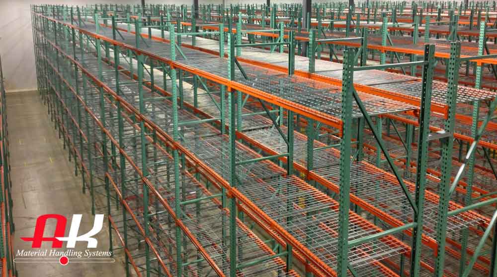 Green and orange pallet racking bays stand tall in. a warehouse each one has wire mesh decking