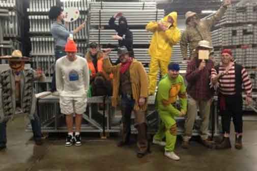 AKMHS Employees Stand on pallet rack beams in the warehouse wearing a variety of fun costumes