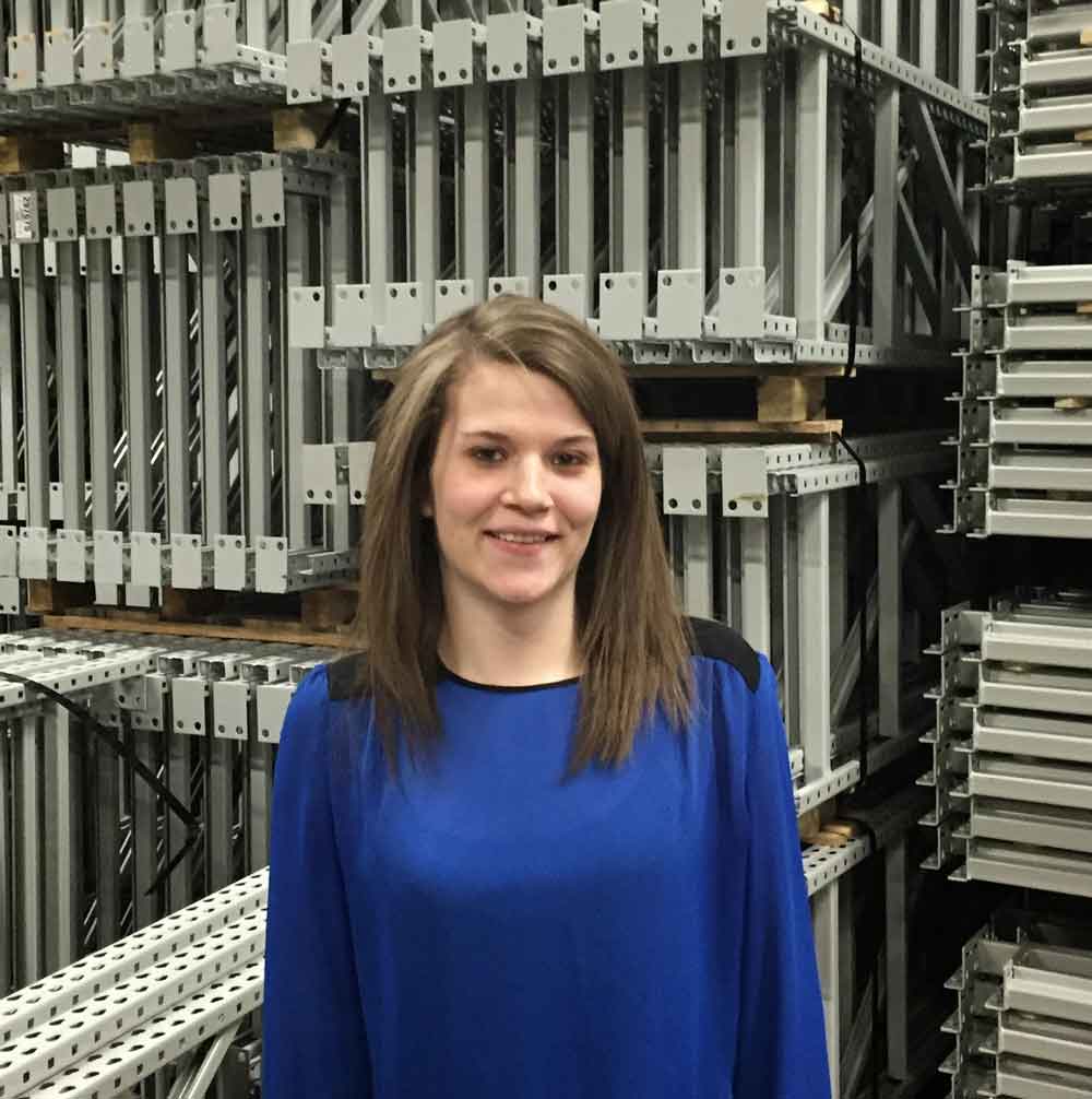AK Employee Tessa Peterson standing in front of stacks of pallet rack frames