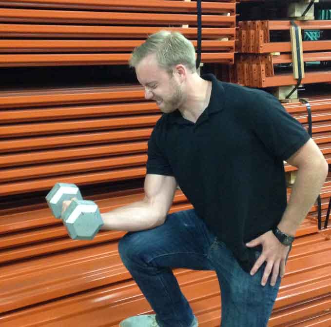 AK Employee lifts a dumbell in front of a row of pallet rack beams