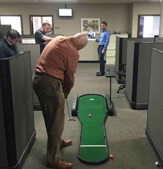 A putting green sits between cubicles as an employee practices their putting