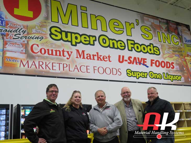 A group of people smile in front of a mienr's poster that's hung in their distribution center
