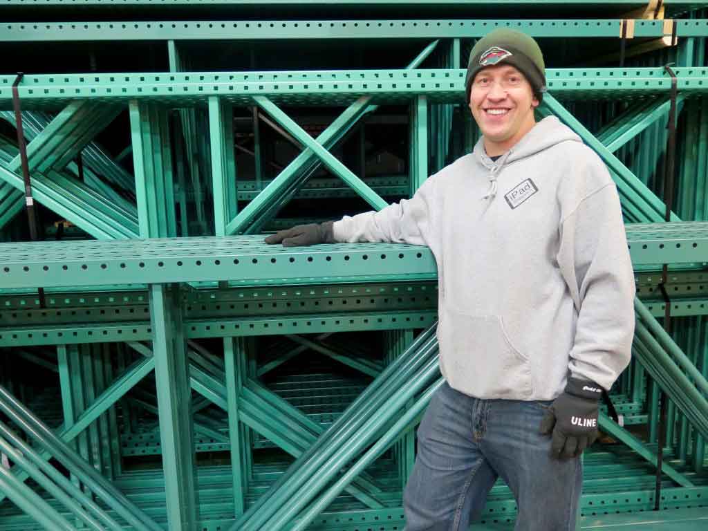 AK employee Eric Dutcher stands and smiles in front of pallet racking frames