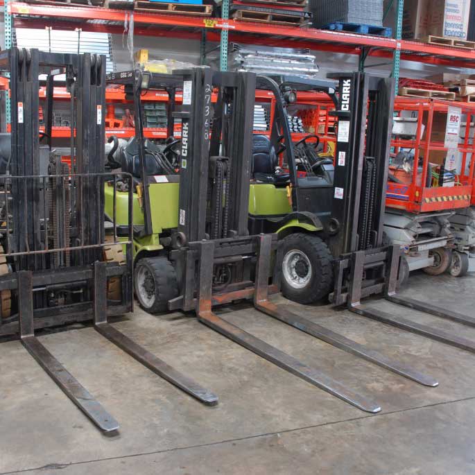 three forklifts and a mobile platform are parked in front of selective pallet racking in a warehouse
