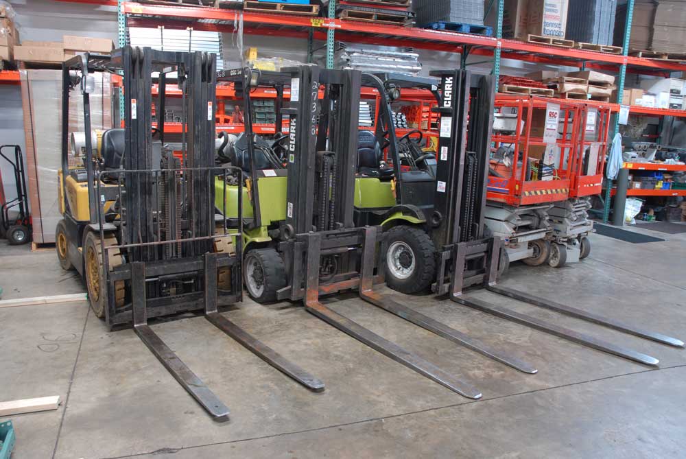 Three forklifts and a mobile platform parked next to each other in front of selective racking in a warehouse