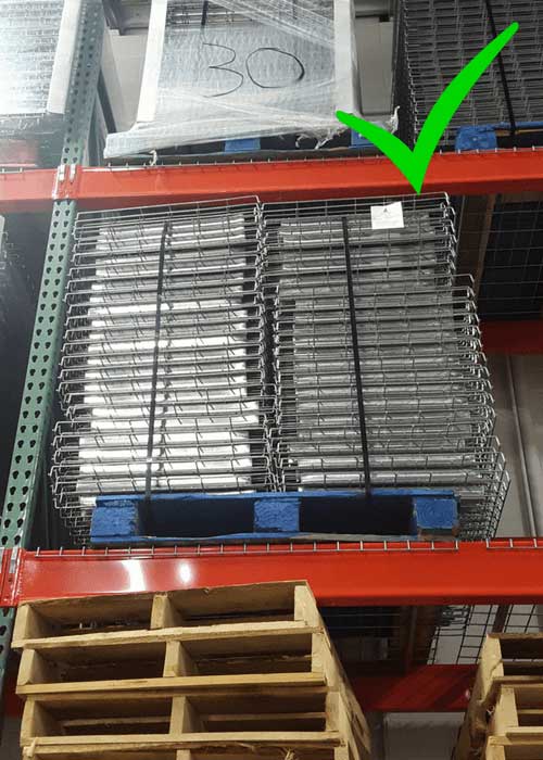 Wire decking stored on a wooden pallet on selective pallet racking with a bright green check mark over the top right corner of the image