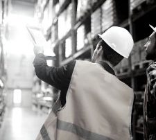 a man in a warehouse wearing a safety hat and vest holding a clipboard