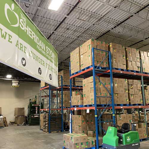 A warehouse with a large green and white sign with pallet racks filled with boxes