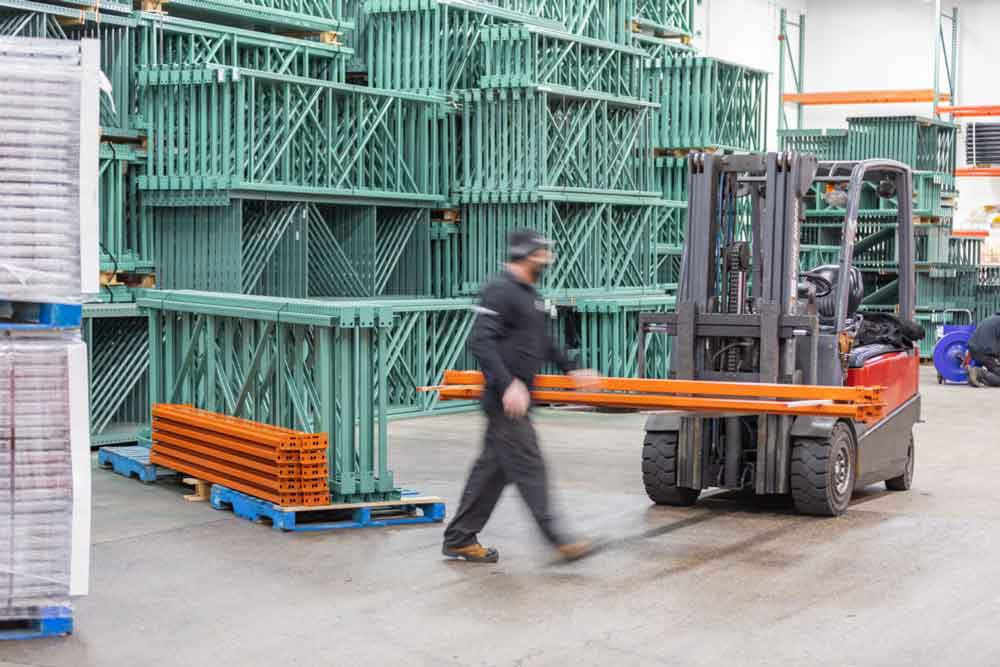 In stock roll form pallet rack frames and beams being packaged by employee in the AK material Handling Systems warehouse.