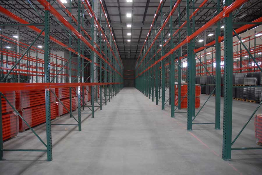 Two aisles of brand new green and orange pallet racking sit in Bunzl’s distribution warehouse. A group of pallet racking beams is seen in the back left corner still wrapped in plastic.