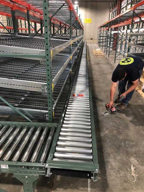 Man installing Carton flow pallet rack and a conveyor belt with additional levels of pallet racking above for replenishment after being freshly installed in a new e commerce warehouse