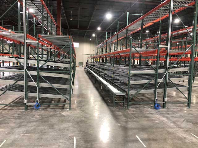 Carton flow pallet rack and a conveyor belt with additional levels of pallet racking above for replenishment after being freshly installed in a new e commerce warehouse