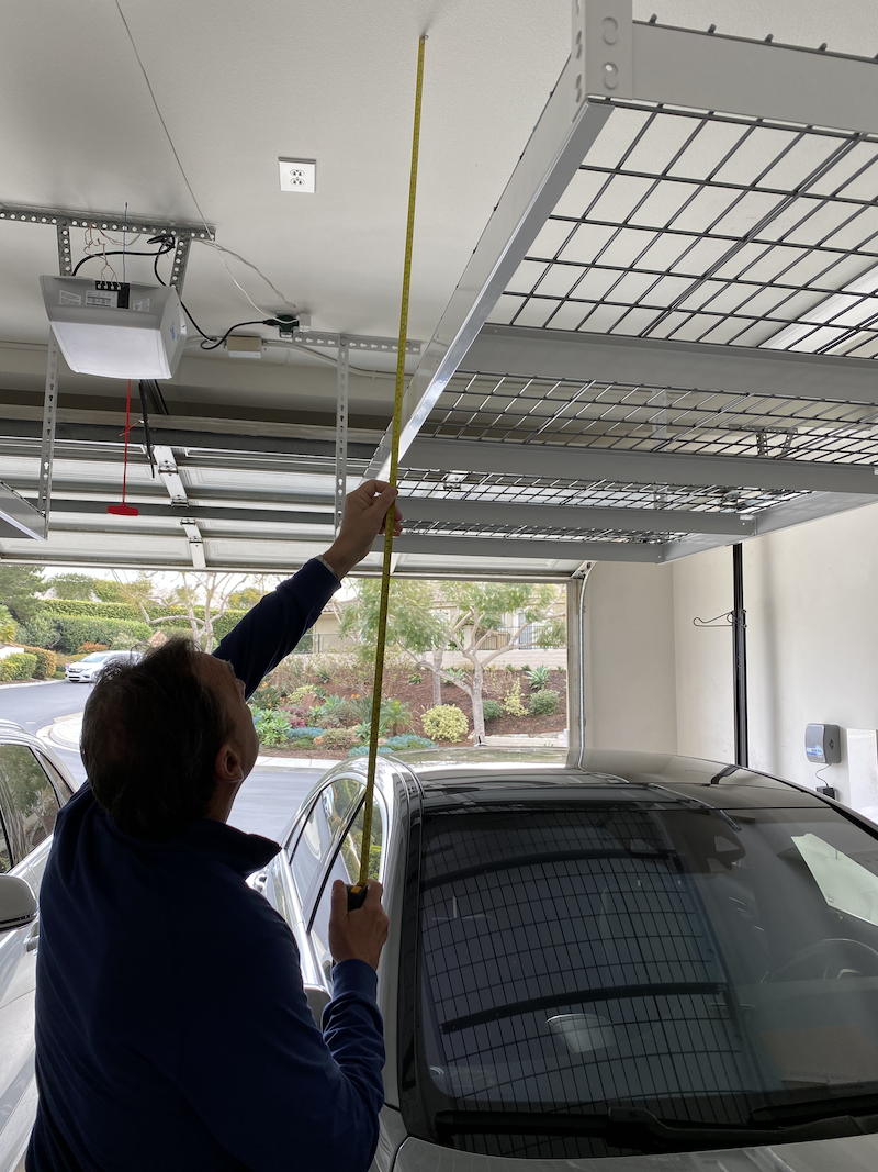 A man measuring a the top of the garage to a the bottom of a hanging metal shelf